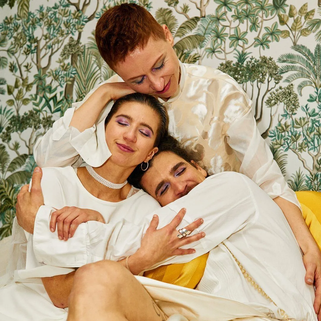 Drei Personen in weiß gekleidet, befinden sich in einer Gruppenumarmung und lachen dabei