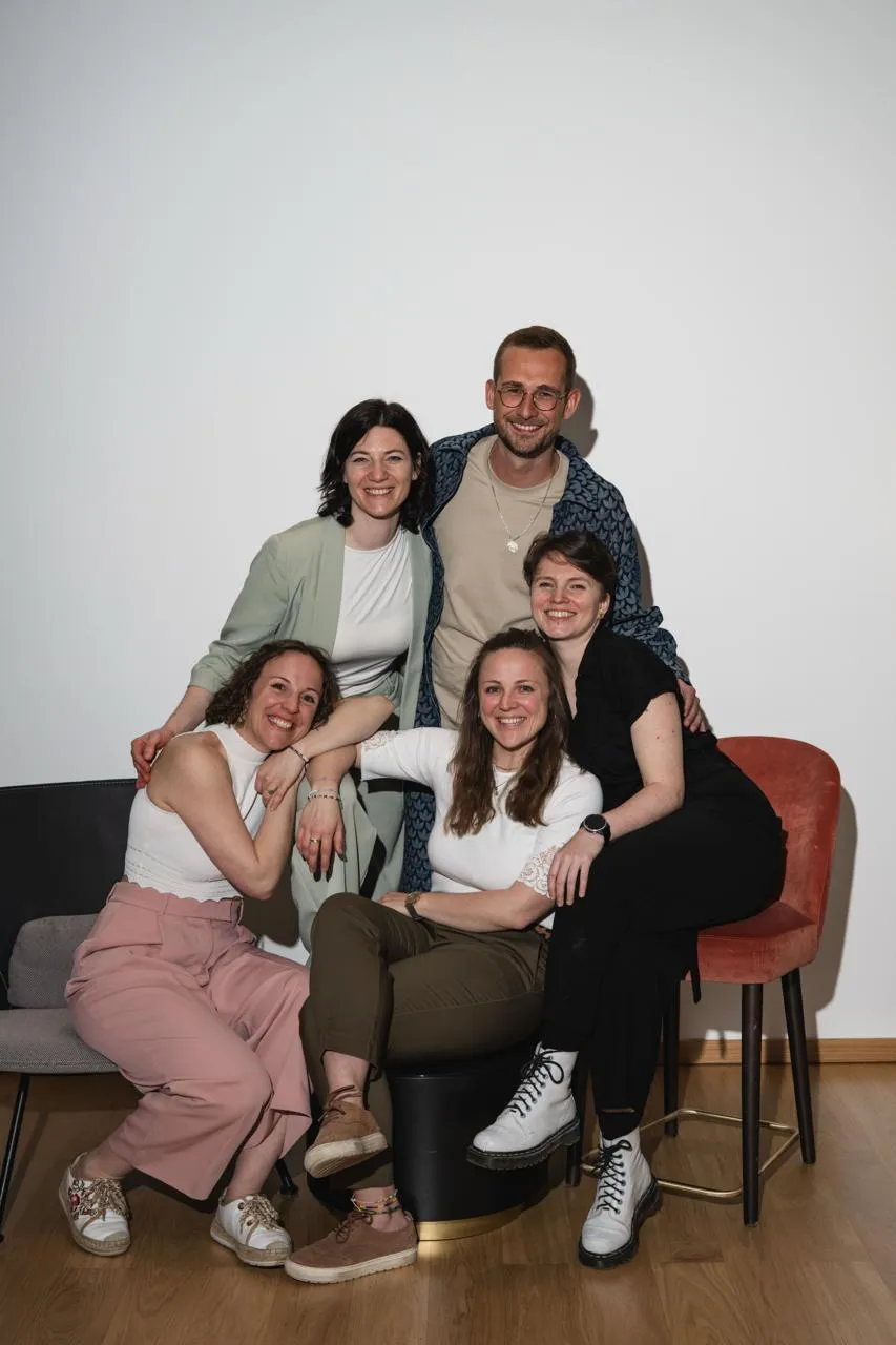 Ein Gruppenfoto von 5 Personen in die Kamera lächeln